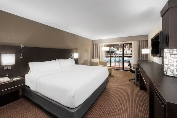 Habitación de hotel con una cama grande, un escritorio, un televisor y vistas a una piscina a través de la puerta de vidrio.
