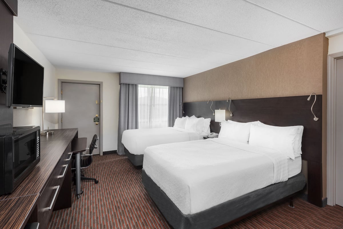 A hotel room with two beds, a desk with a TV, and a minibar.