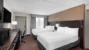 A hotel room with two beds, a desk with a TV, and a minibar.