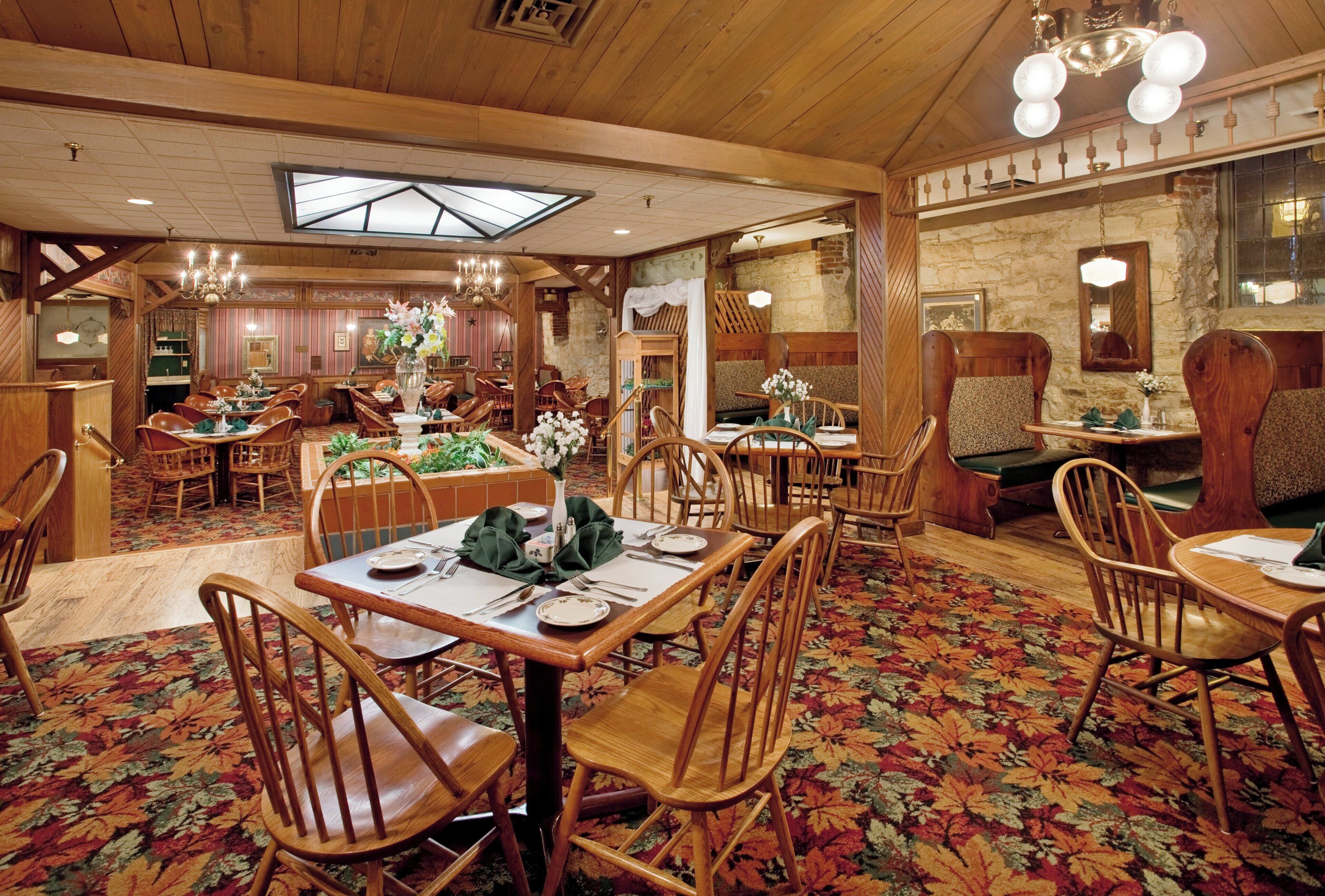 A restaurant with wooden furniture, a floral carpet, and a high ceiling with a skylight.