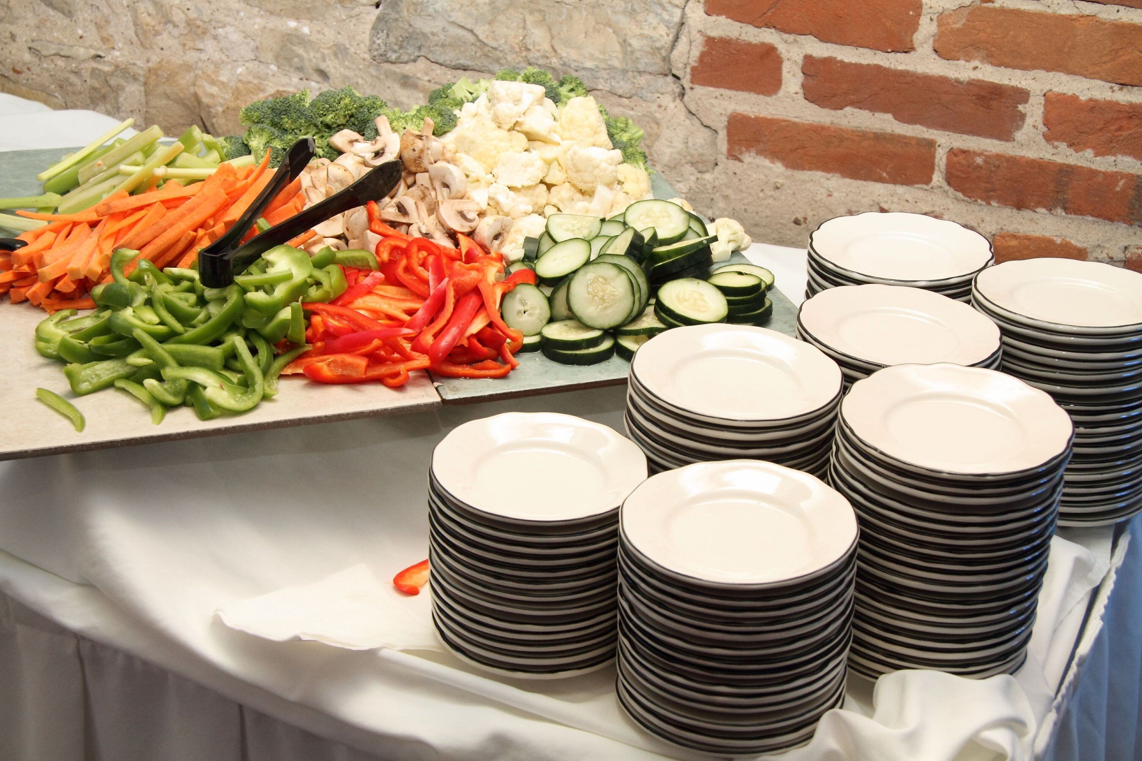 A buffet table with various vegetables and stacks of plates.