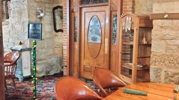 Una habitación con una mesa de madera, sillas de cuero, una pared de piedra, una puerta de madera con un panel de vidrio y un pequeño abeto navideño.