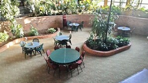 Ein möblierter Patio-Bereich mit runden Tischen und Stühlen, umgeben von Ziegelmauern und Kübelpflanzen.