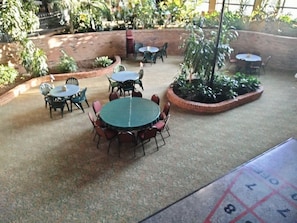 Un patio al aire libre con varias mesas y sillas redondas, rodeado de muros de ladrillo y plantas en macetas.