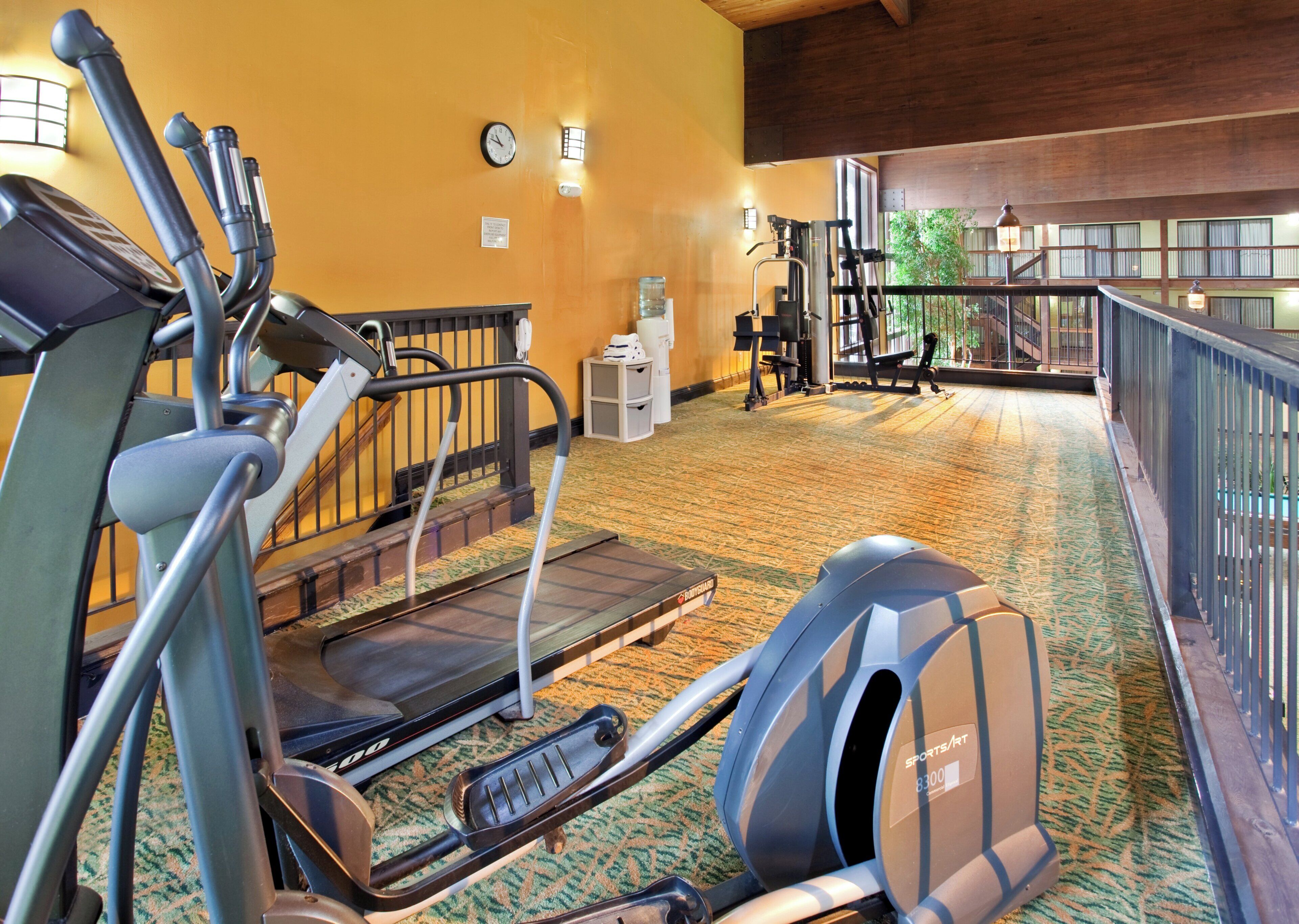 Une salle de sport équipée de matériel d’exercice, avec une horloge et un distributeur d’eau.