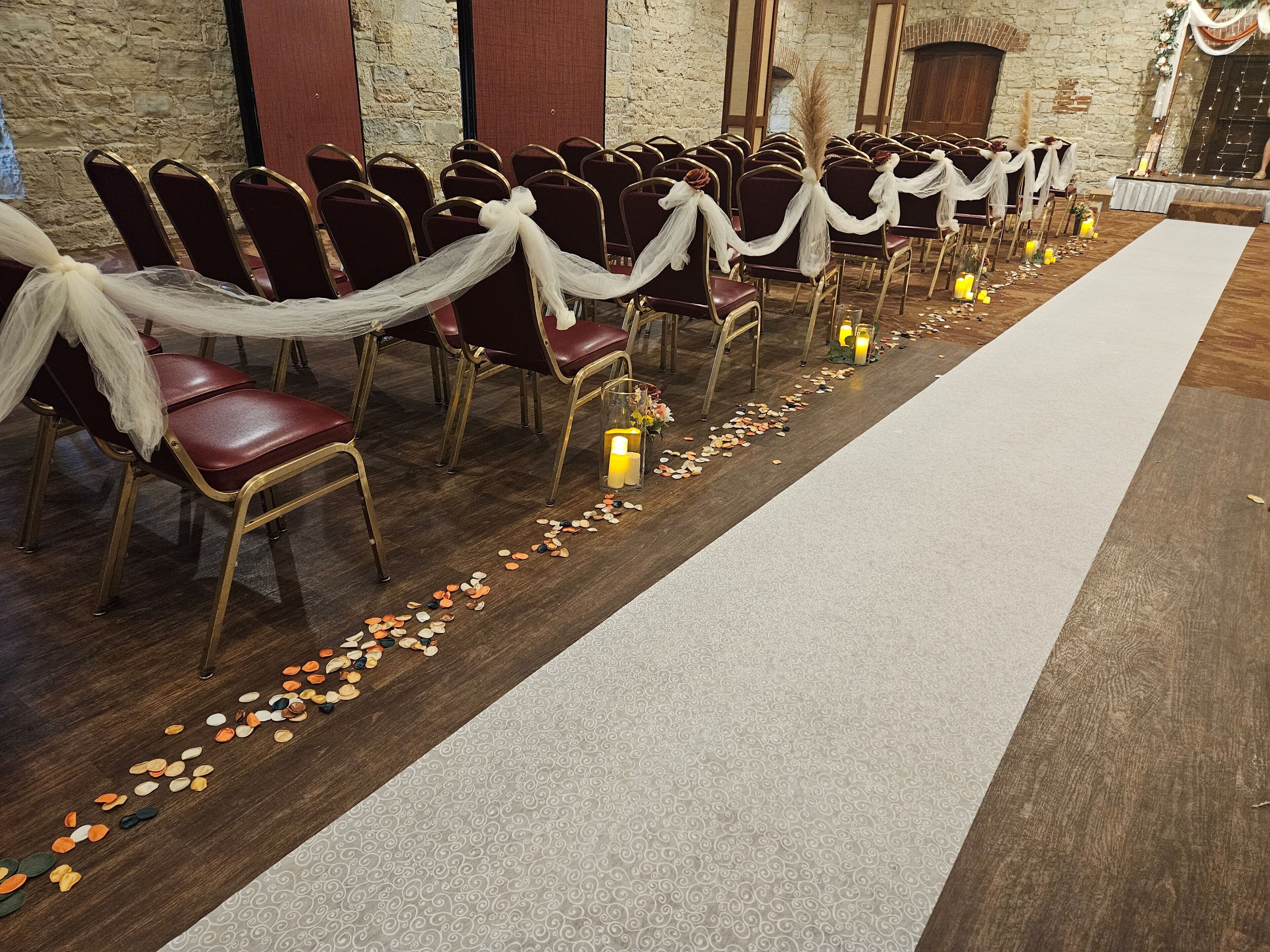 Des rangées de chaises drapées de tissu blanc, une allée recouverte de moquette et des bougies disposées le long du chemin.