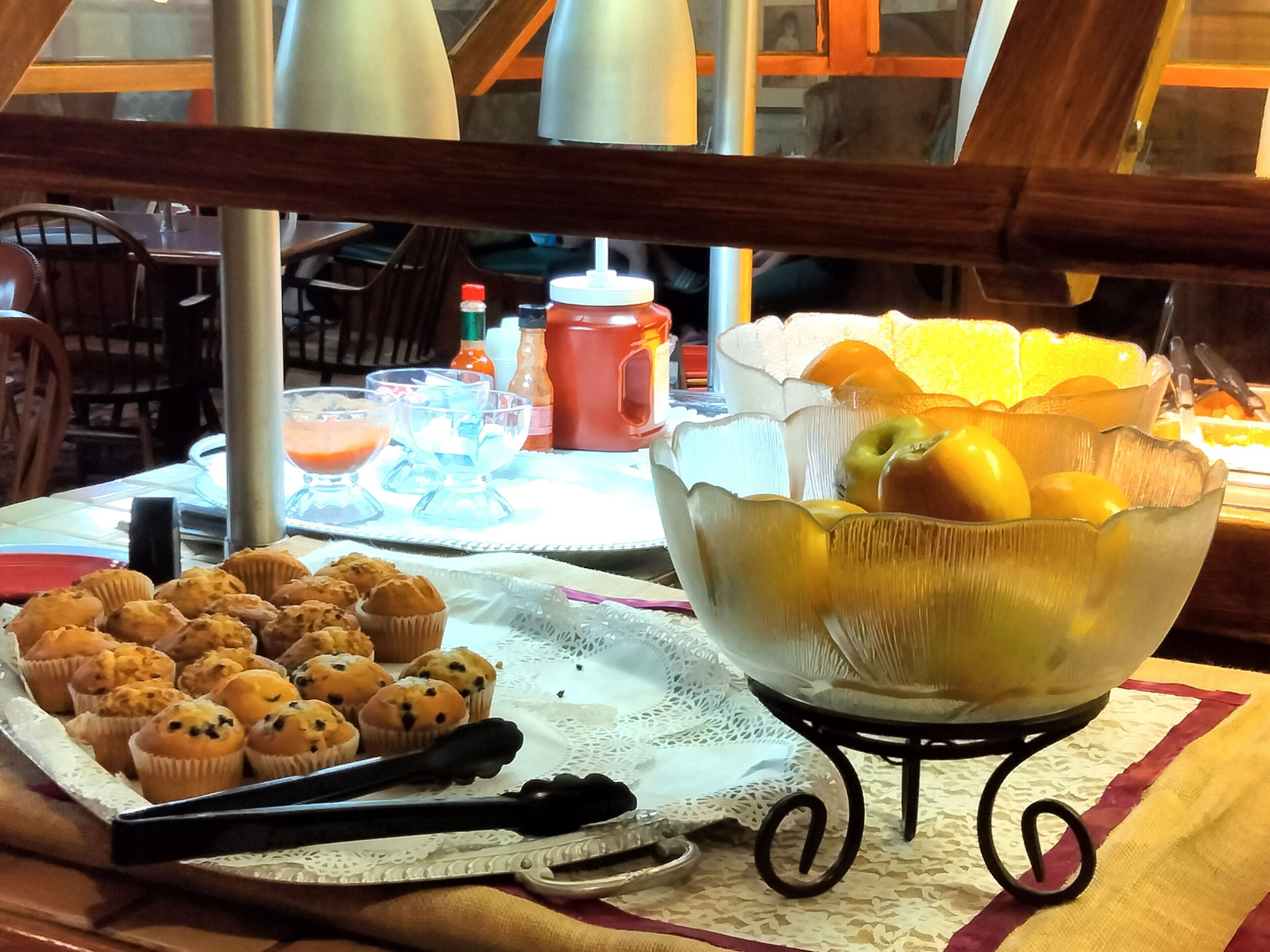 A breakfast table with muffins, a fruit bowl, and condiments.