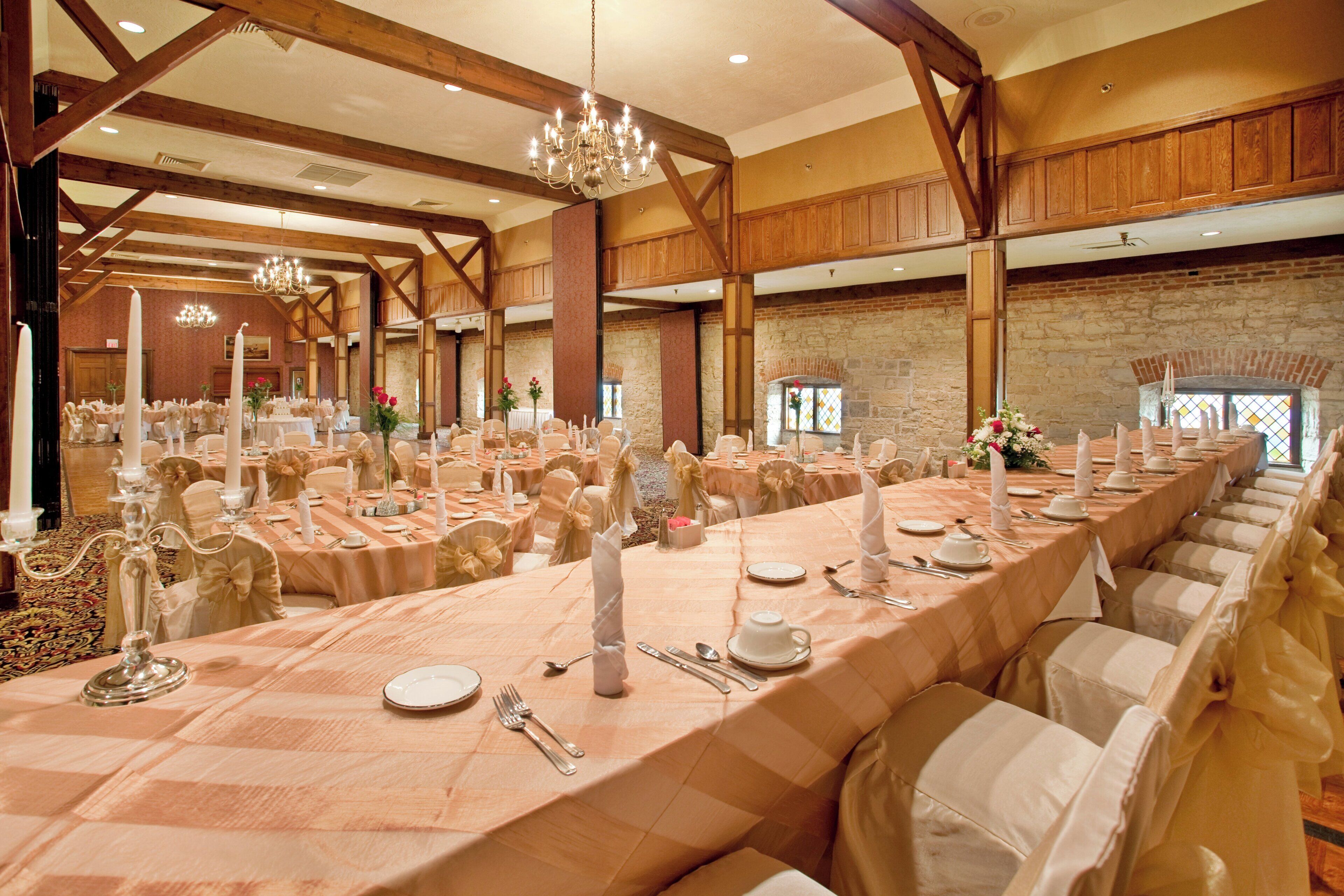 Un salón de banquetes con largas mesas dispuestas para un evento formal, con candelabros y paredes de piedra.