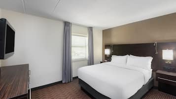 Habitación de hotel con una cama grande, un televisor montado en la pared, un escritorio con una silla y una ventana con cortinas.