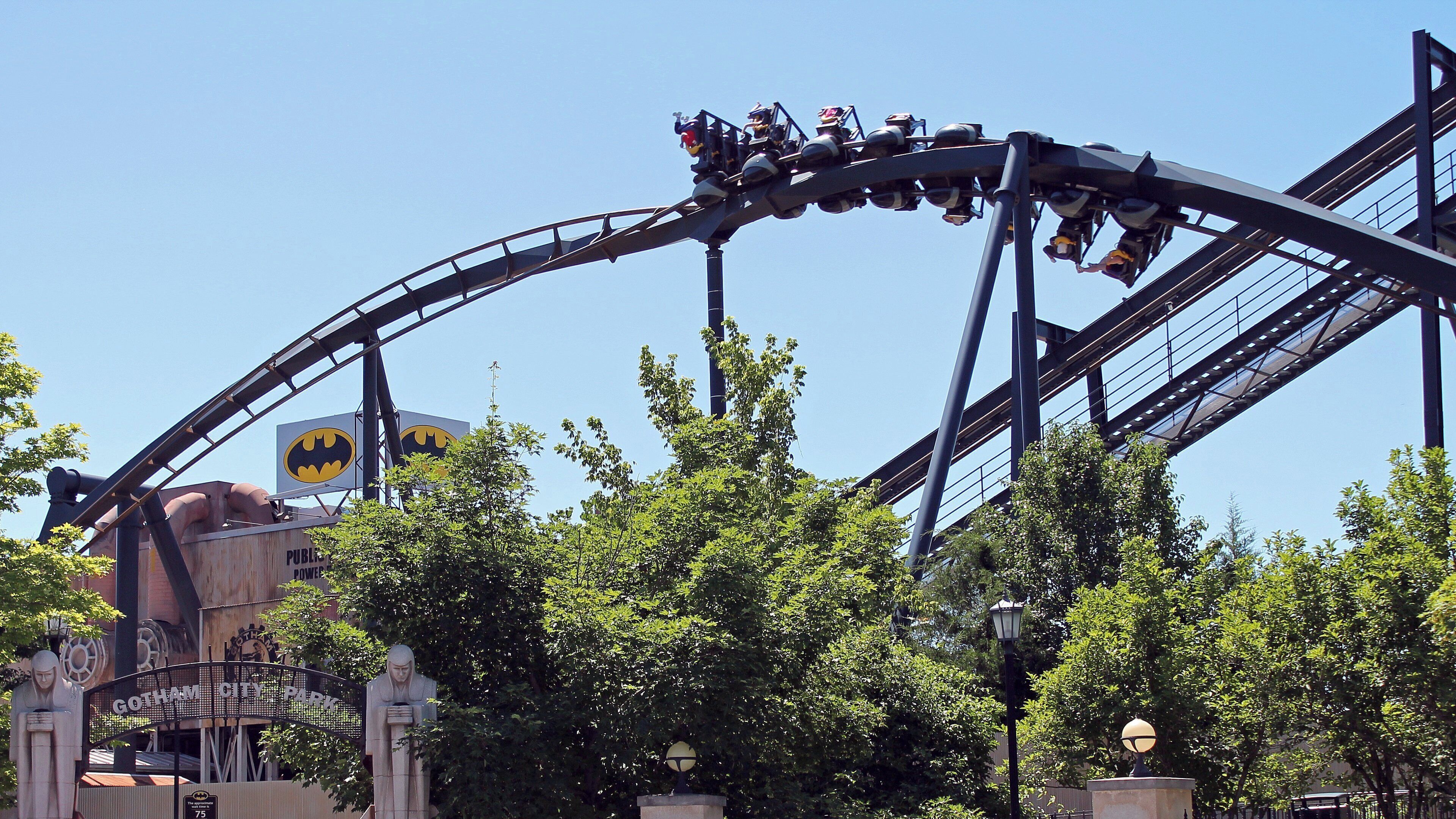 Eine Achterbahn mit Batman-Logo, umgeben von Bäumen und einer Batman-Statue.