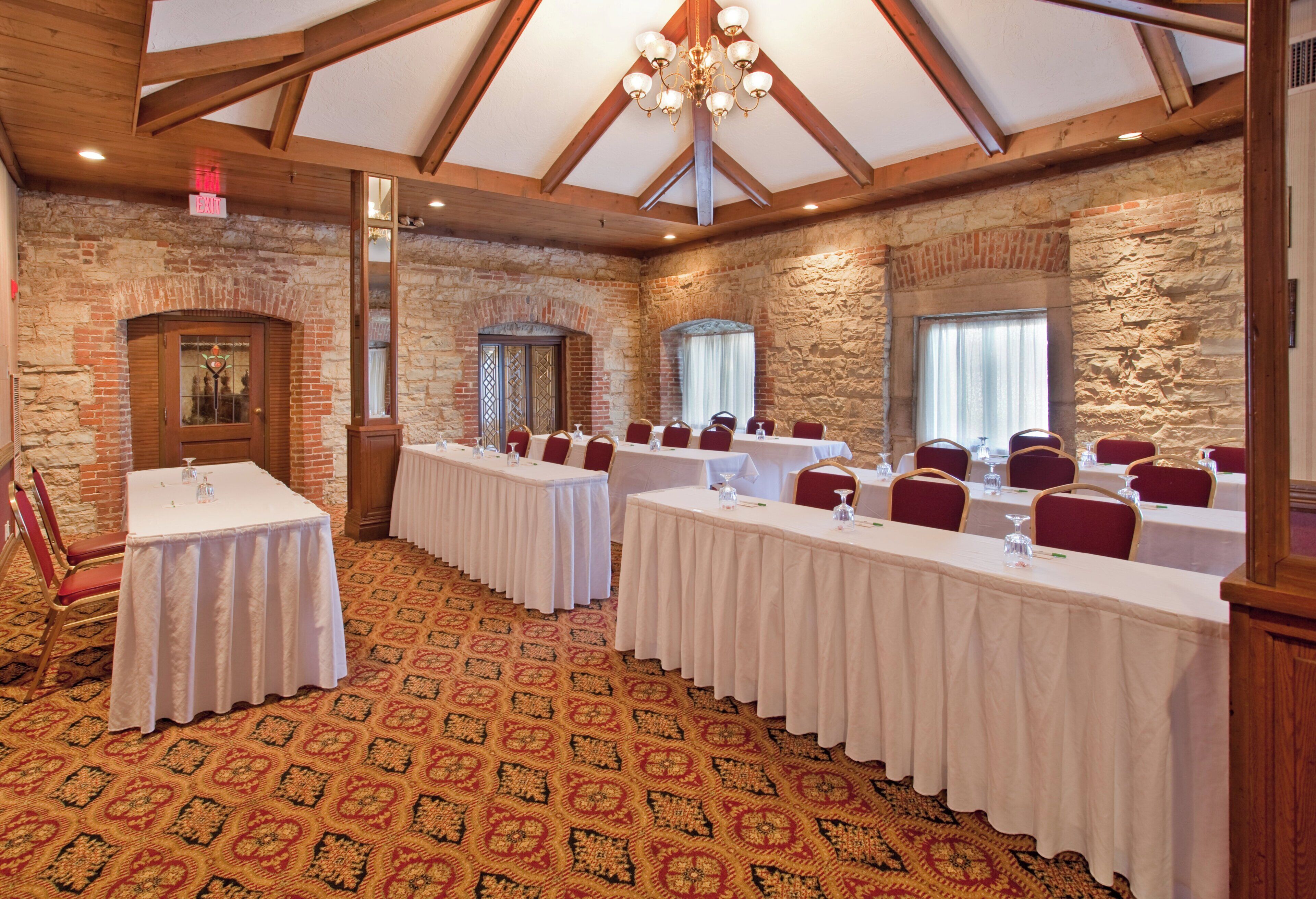 Une salle de conférence avec de longues tables, des chaises rouges et un tapis à motifs.