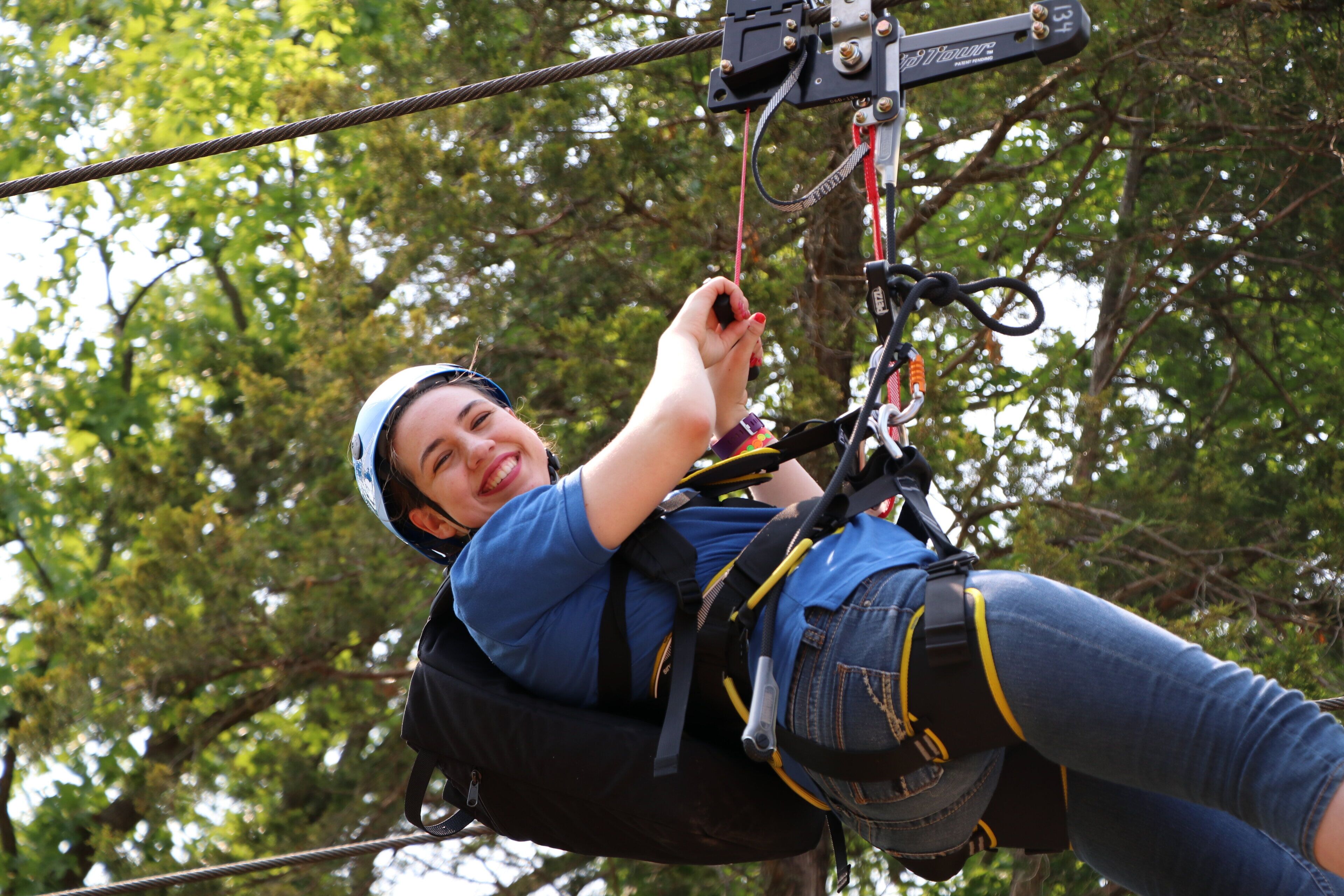 A person engaged in an outdoor activity, secured with harnesses and ropes, surrounded by trees.