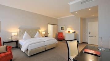 A hotel room with a bed, a desk, a chair, a red armchair, and a lamp.