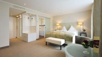 A hotel room with a bed, bedside table, lamp, and a glass table with a vase of flowers.