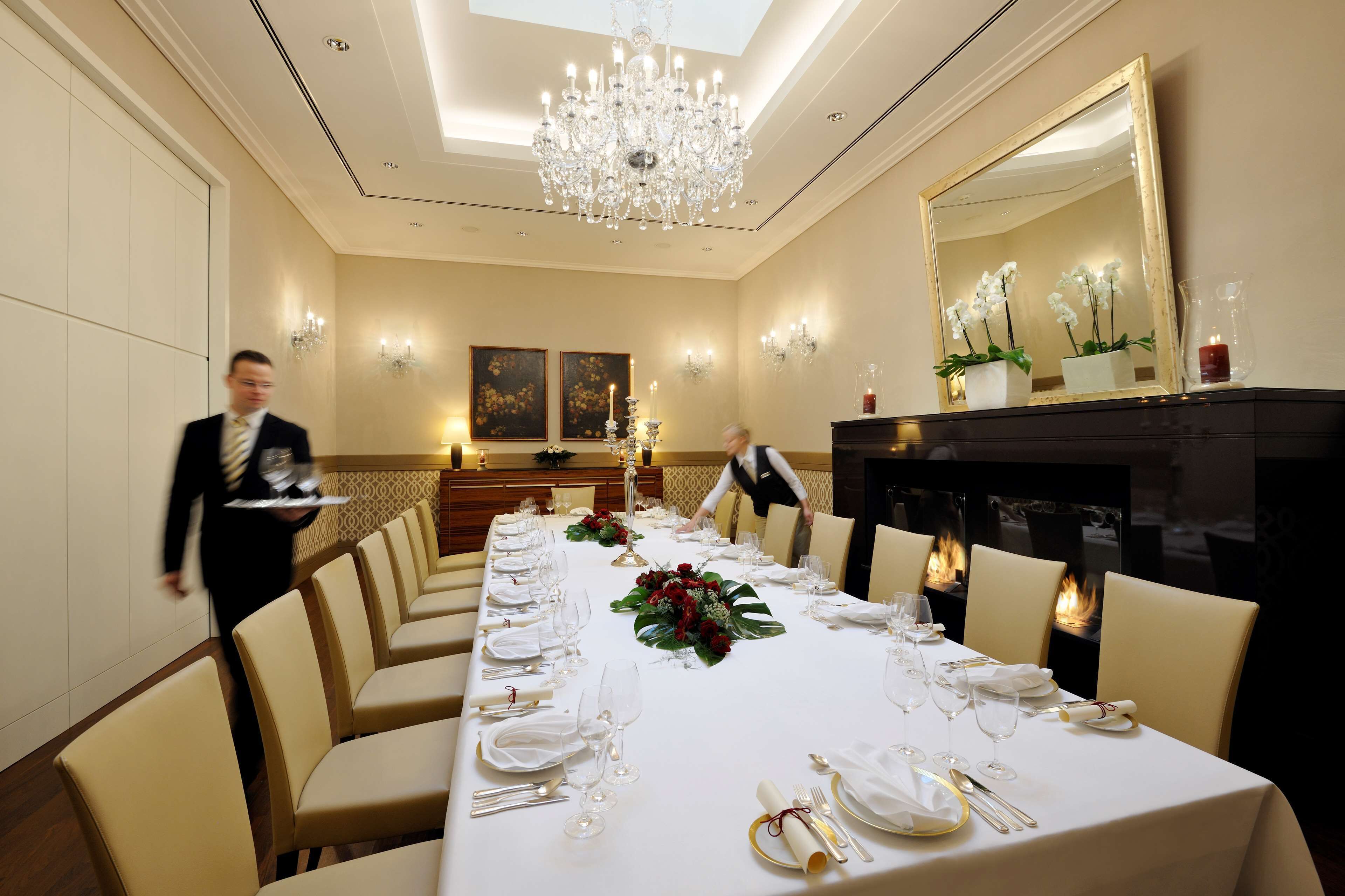 Een goed verlichte balzaal met een lange tafel gedekt voor een formeel evenement, een kroonluchter en een open haard.
