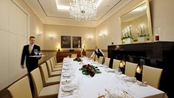 Een goed verlichte balzaal met een lange tafel gedekt voor een formeel evenement, een kroonluchter en een open haard.