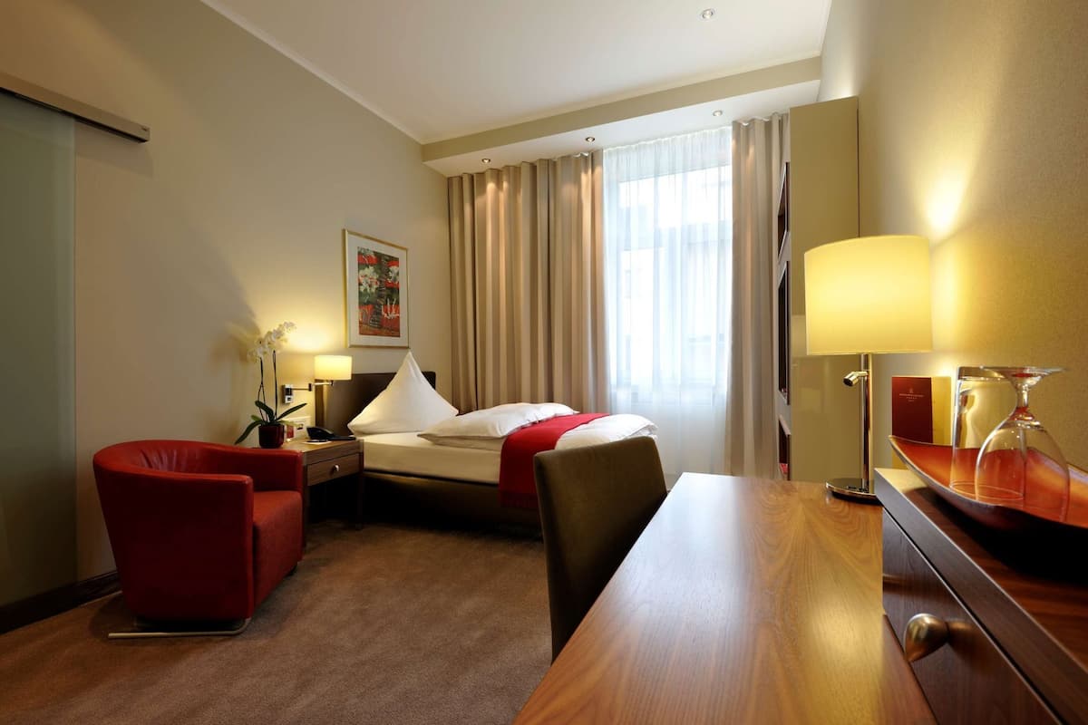 Hotelkamer met een bed, bureau, stoel, lamp, televisie en raam met gordijnen.