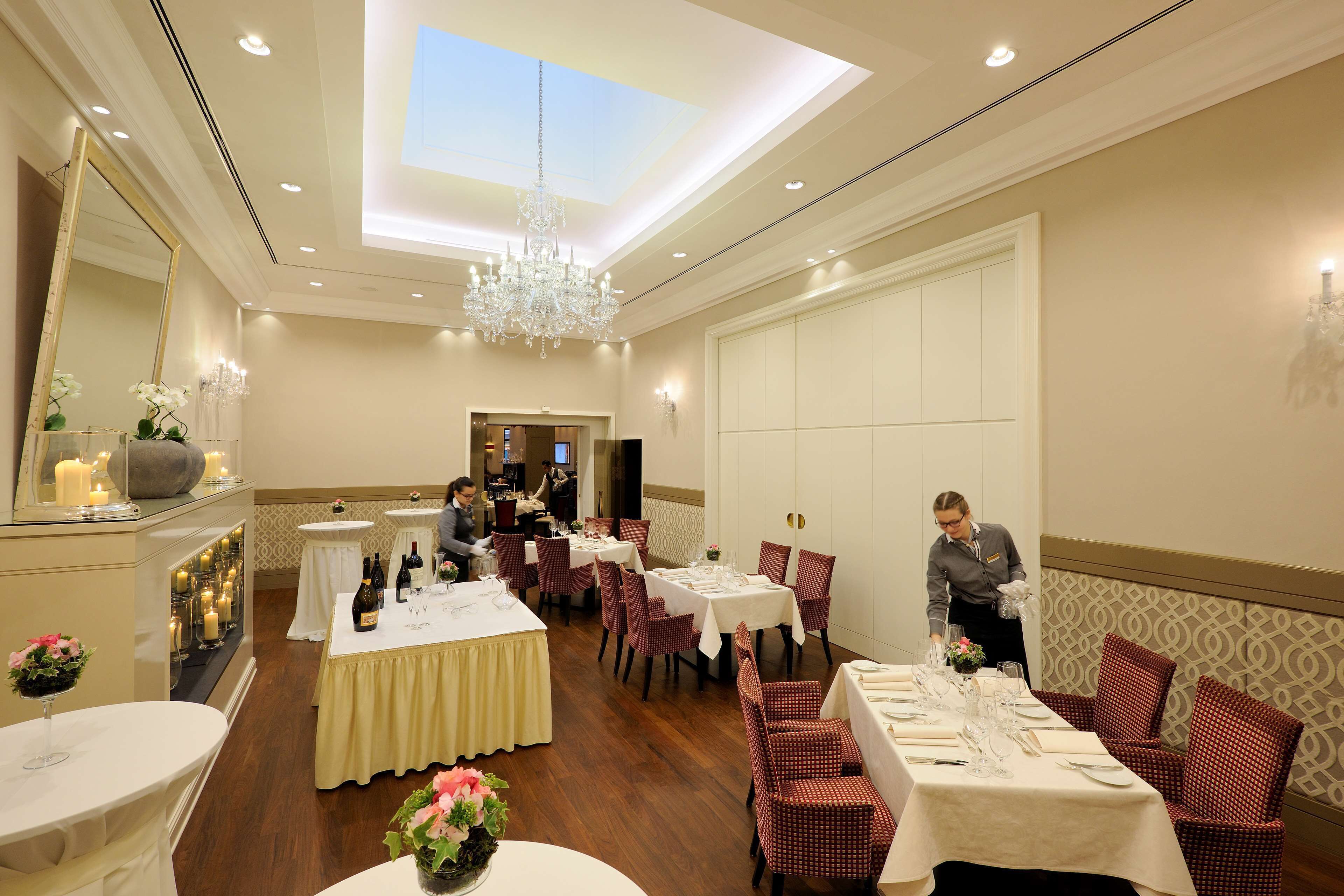 Ein Speisesaal eines Hotels mit gedeckten Tischen, einer Kandelaber und einem Oberlicht.