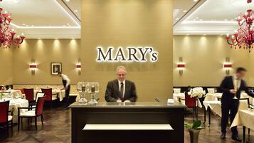 Eine Rezeption mit einem Schild, auf dem 'MARY'S' steht, in einer Hotelhalle mit für Gäste bereitgestellten Tischen und Stühlen.