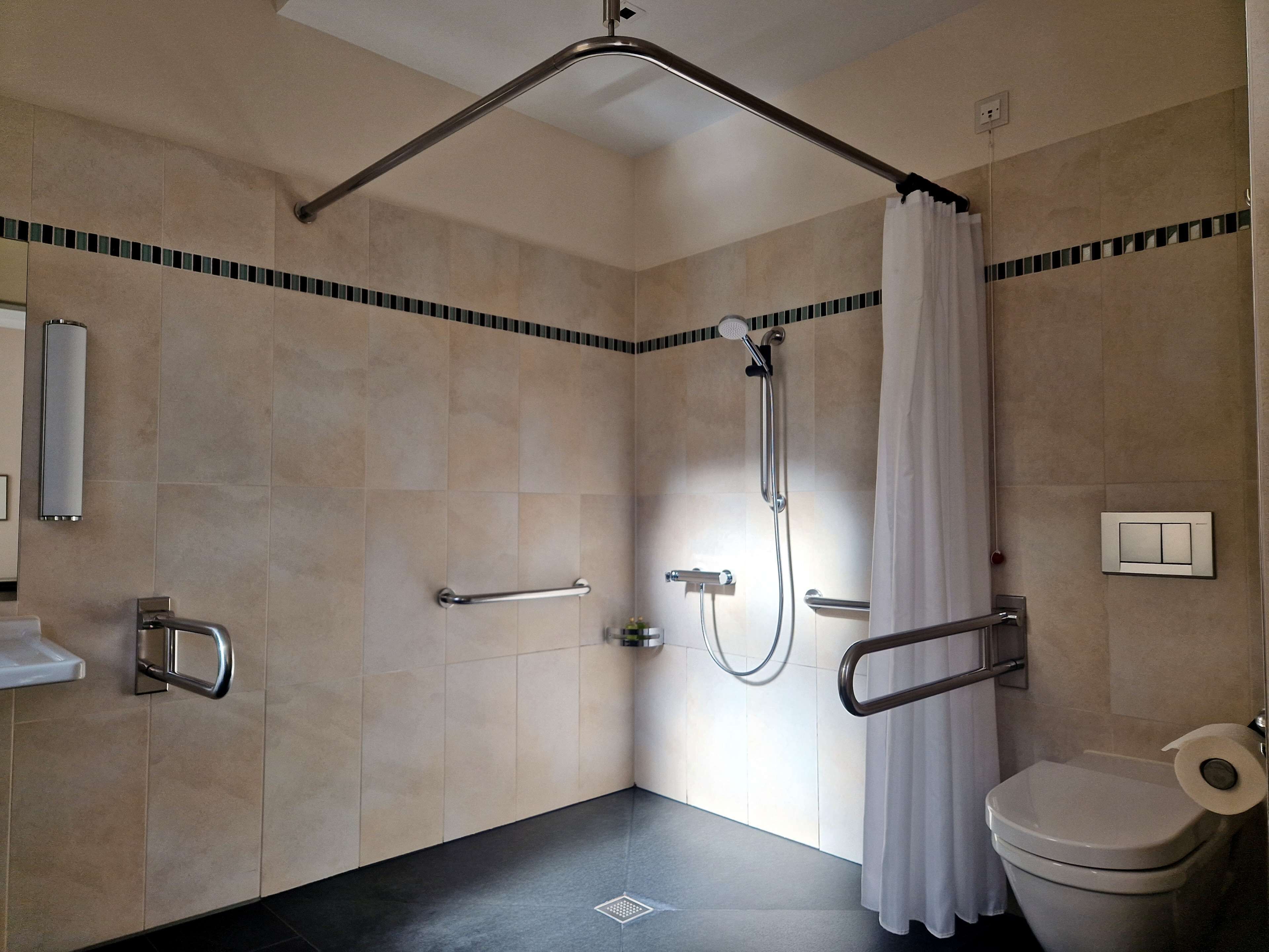 A modern bathroom with a shower, toilet, and handrails.