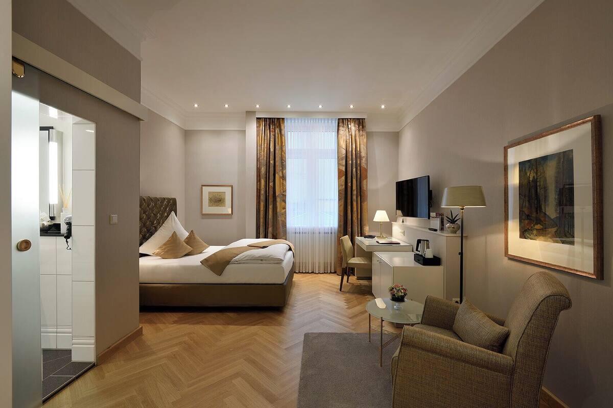 Een hotelkamer met een bed, bureau, stoel, televisie en kunstwerk.