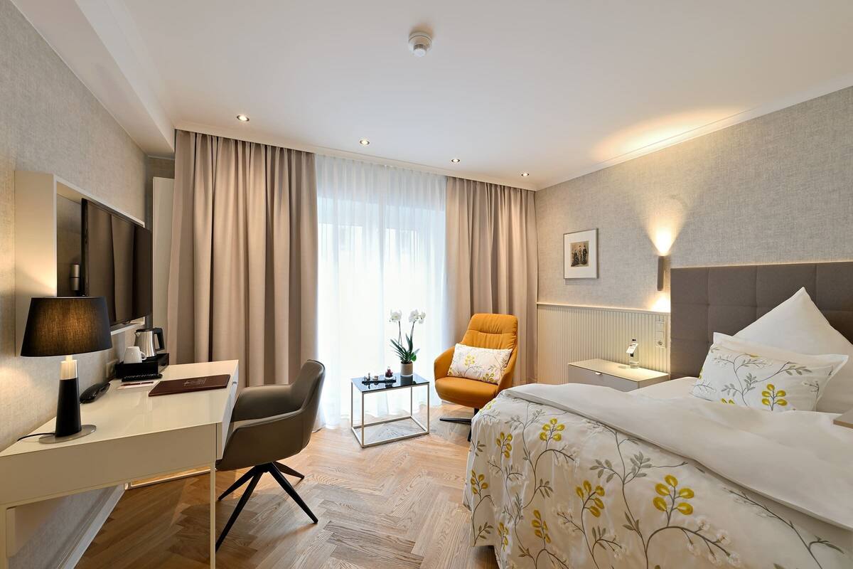 Een hotelkamer met een bed, een bureau, een stoel, een nachtkastje en een raam met gordijnen.