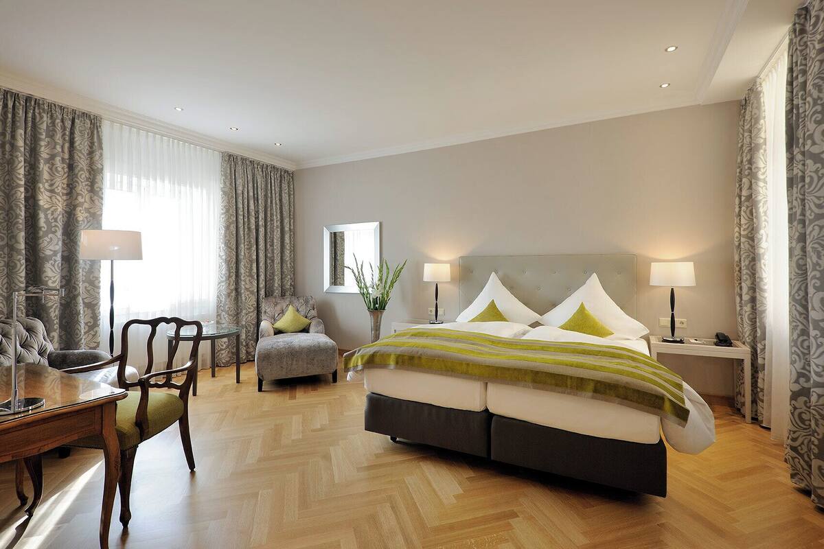 Een hotelkamer met een groot bed, twee nachtkastjes, een stoel, een bureau en een spiegel.