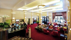 En rymlig entréhall med en röd matta, flera sittgrupper och en receptionsdisk med datorer.
