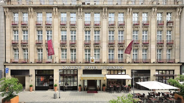 En historisk byggnad med en klassisk fasad, flera balkonger med blomlådor och en framträdande entré med en skylt som lyder "Kastens Hotel Luisenhof".