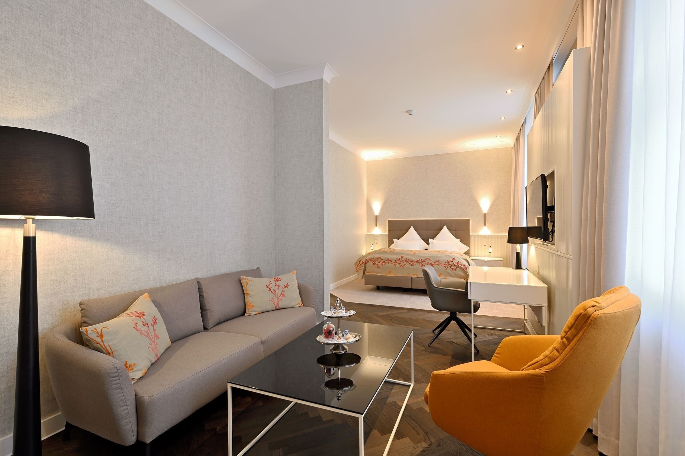 Quarto de hotel moderno com sofá, poltrona e uma mesinha com um tabuleiro de objetos.