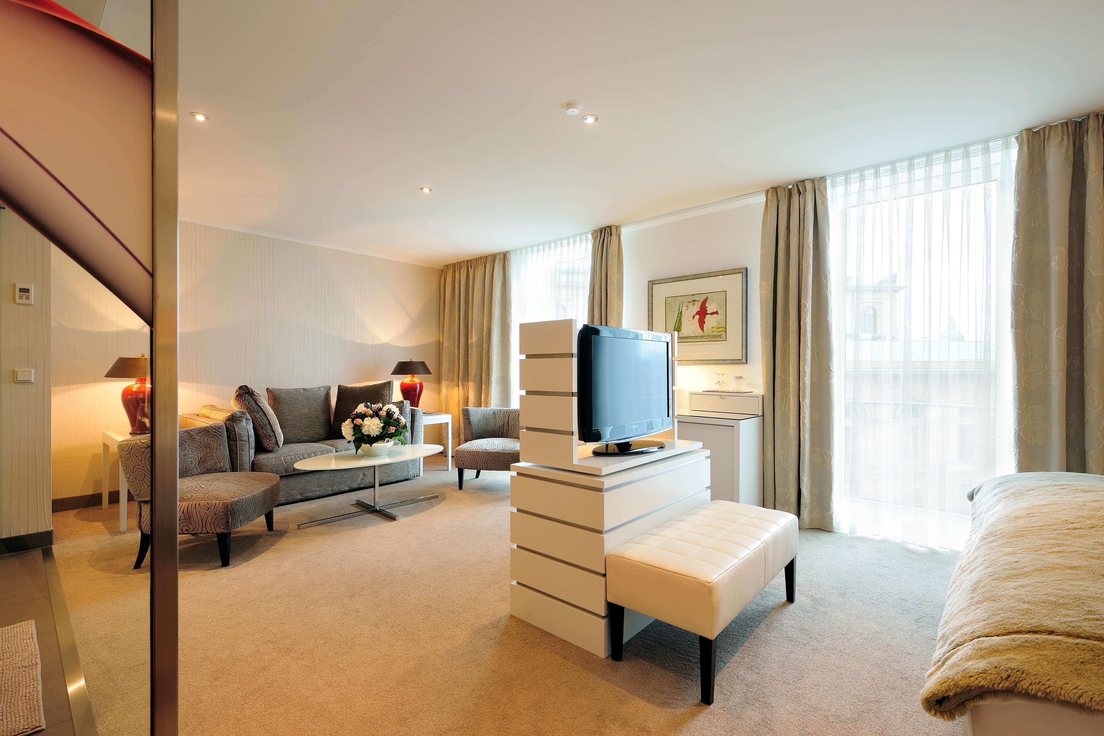 Una habitación de hotel moderna con sofá, televisión, cama y escritorio con lámpara.