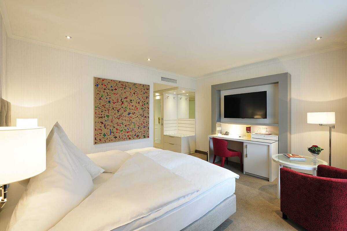 Een hotelkamer met een bed, een bureau, een televisie en een rode stoel.