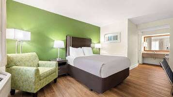Una habitación de hotel con una cama grande, una pared de acento verde, piso de madera, una silla y una mesita de noche con lámparas.