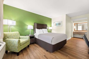 Una habitación de hotel con una cama grande, una pared de acento verde, piso de madera, una silla y una mesita de noche con lámparas.