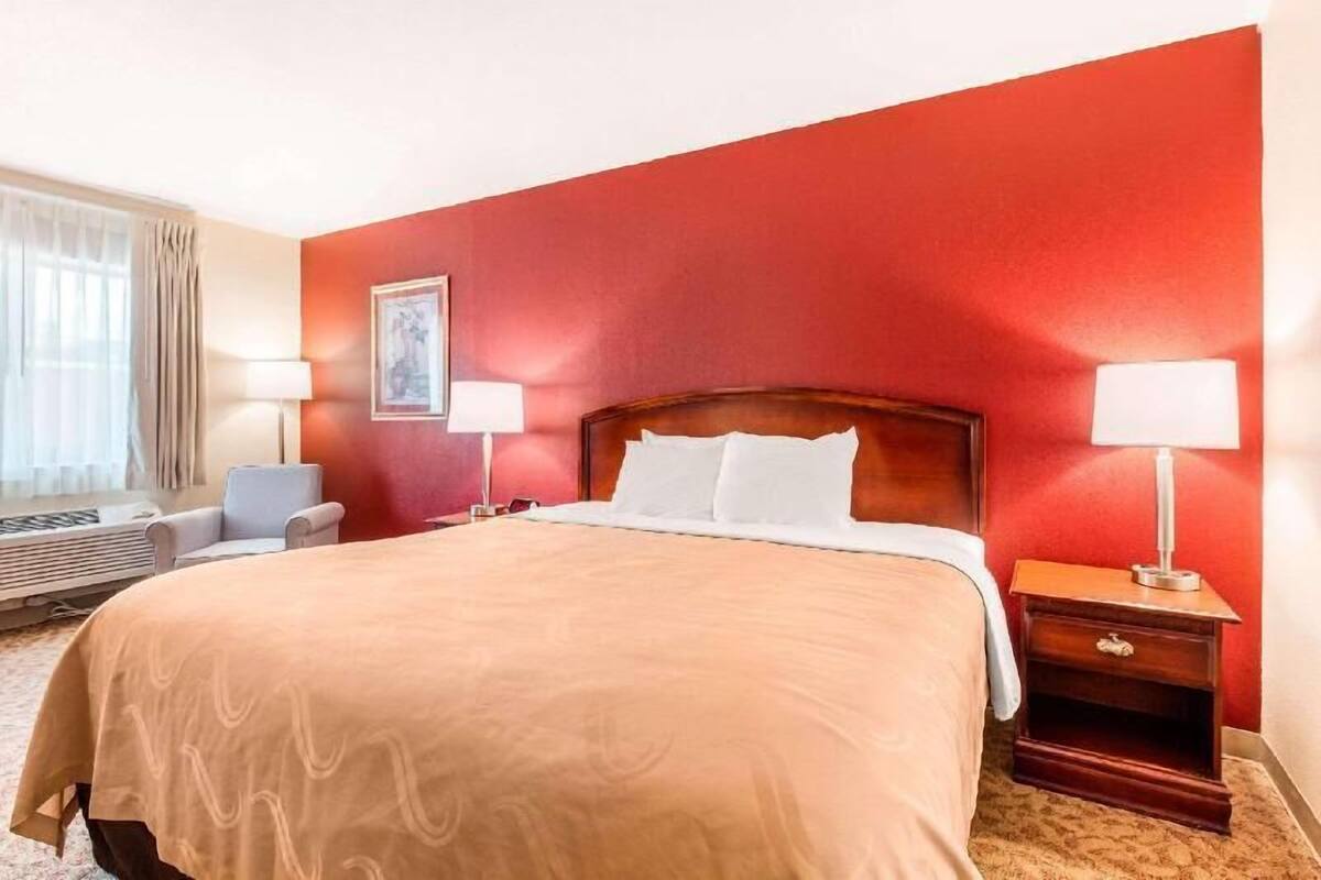 A hotel room with a large bed, two bedside lamps, a chair, and a picture on the wall.