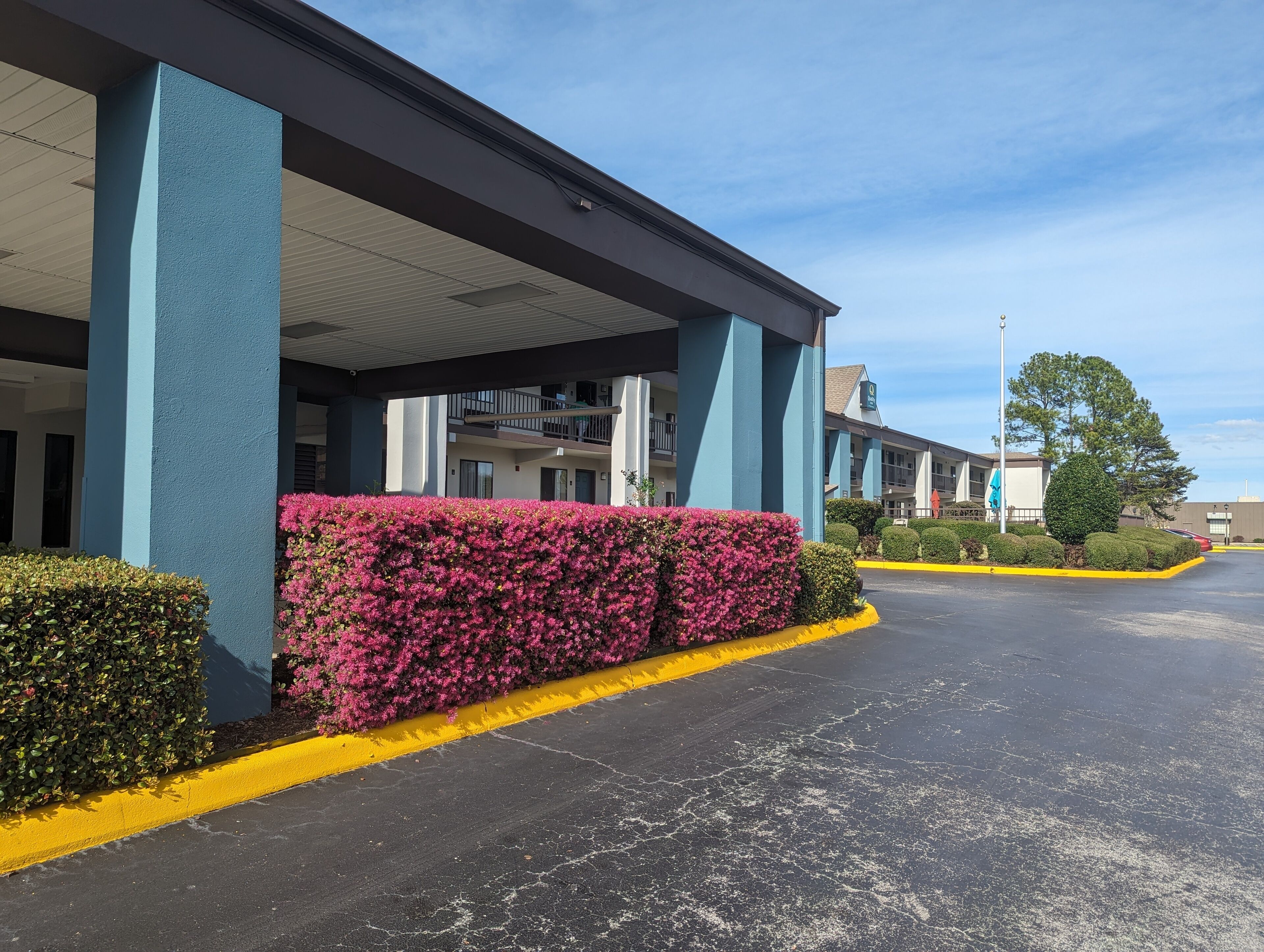 A hotel with a covered entrance, a parking lot, and a building with balconies.