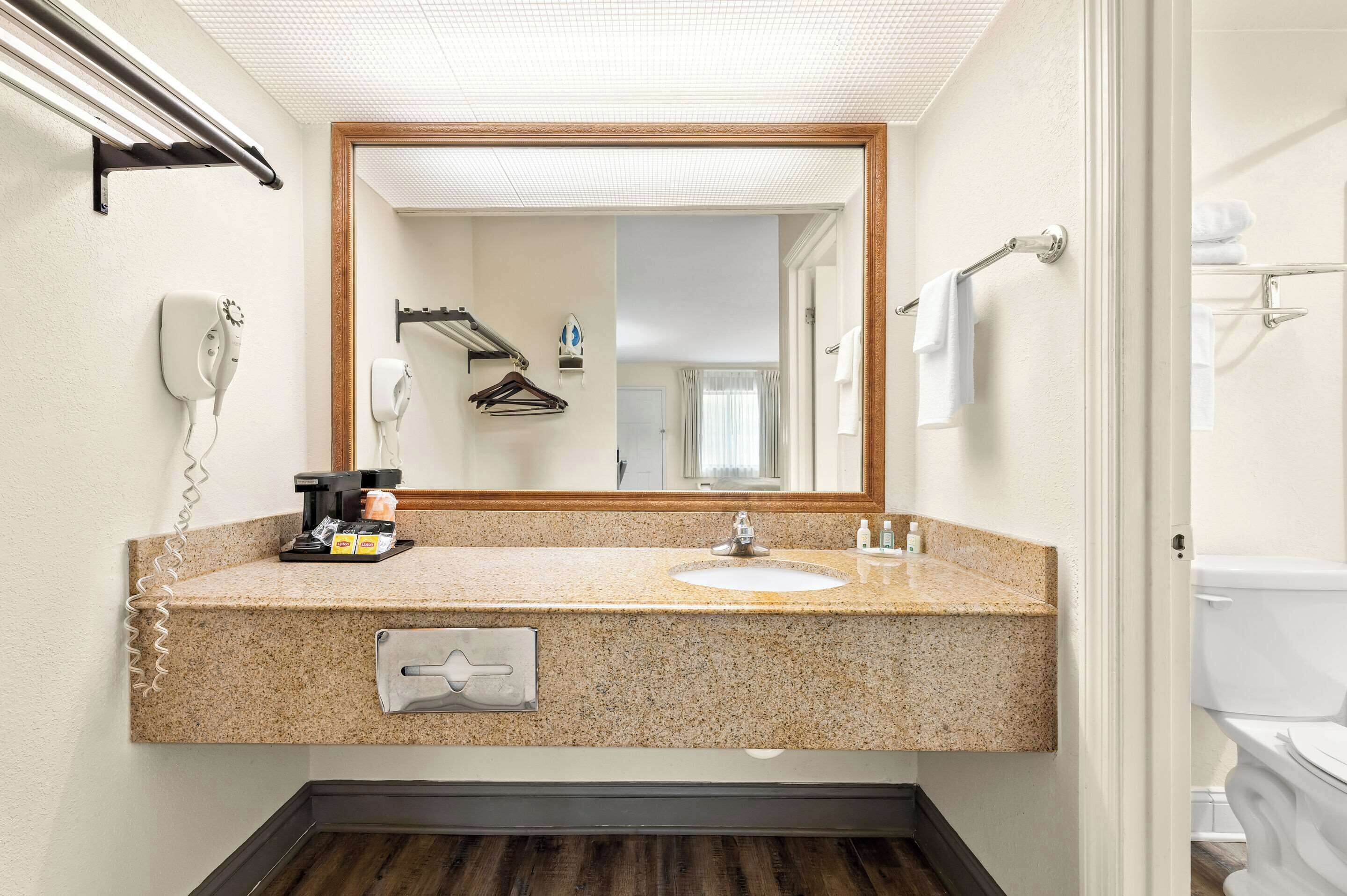 A bathroom with a granite countertop sink, a mirror, a hairdryer, and a towel rack.