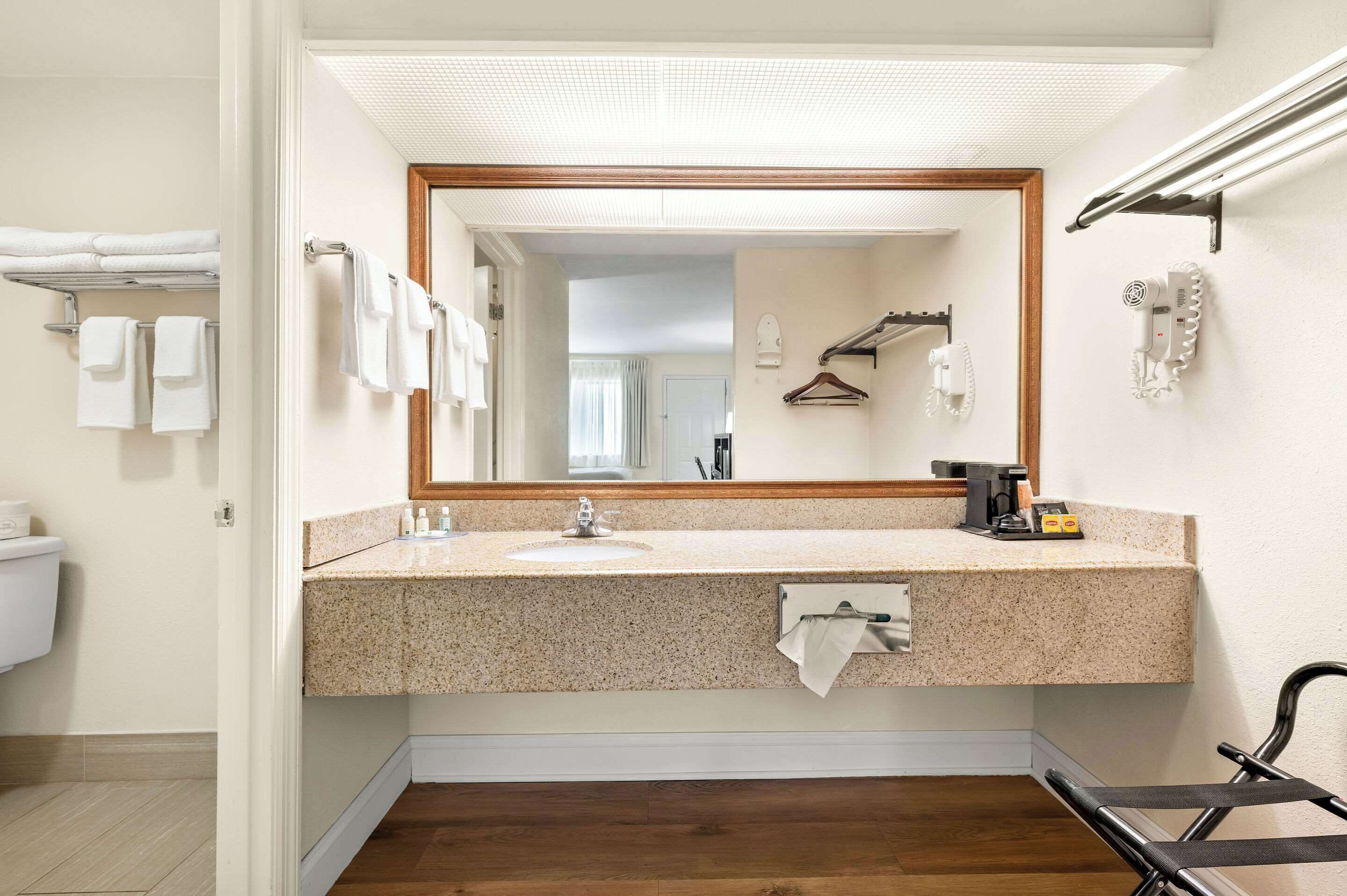 A bathroom with a granite countertop sink, a mirror with a wooden frame, a towel rack, and a hairdryer mounted on the wall.