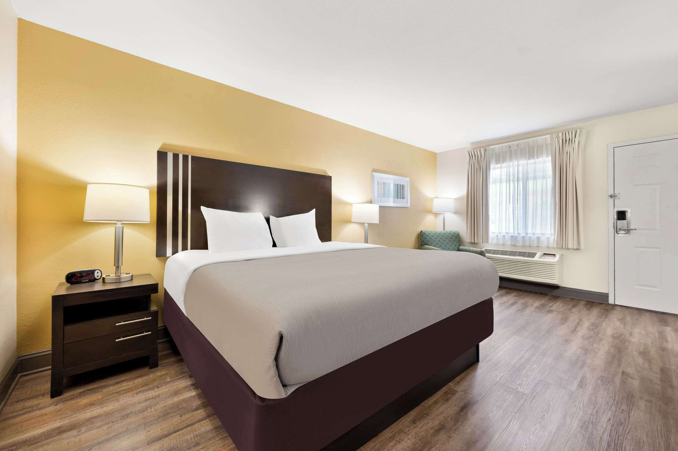 A hotel room with a large bed, bedside tables with lamps, a wall-mounted air conditioner, and a door with a handle.
