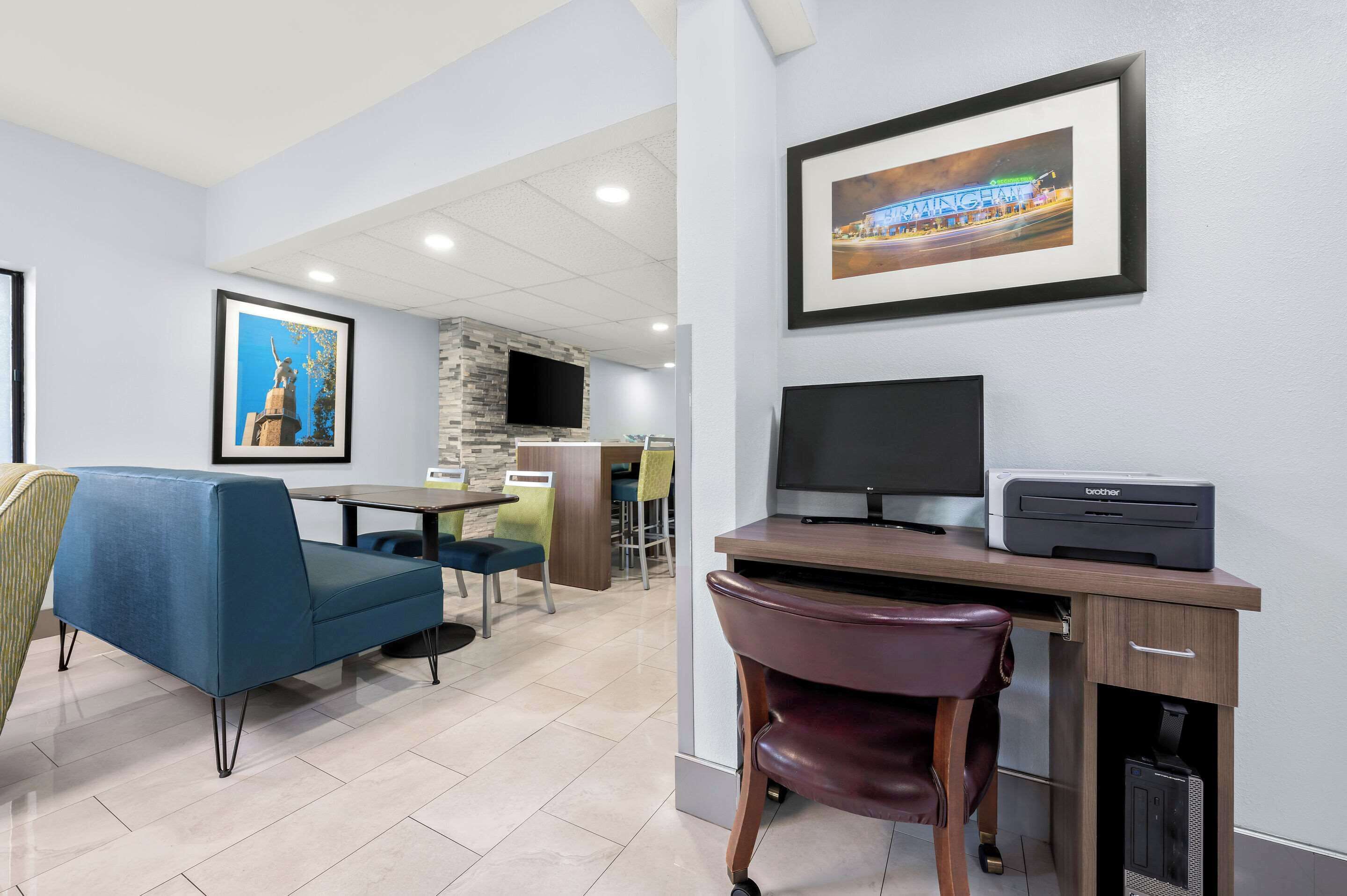 Habitación de hotel con sofá azul, un escritorio de madera con una impresora, un televisor y cuadros en la pared.