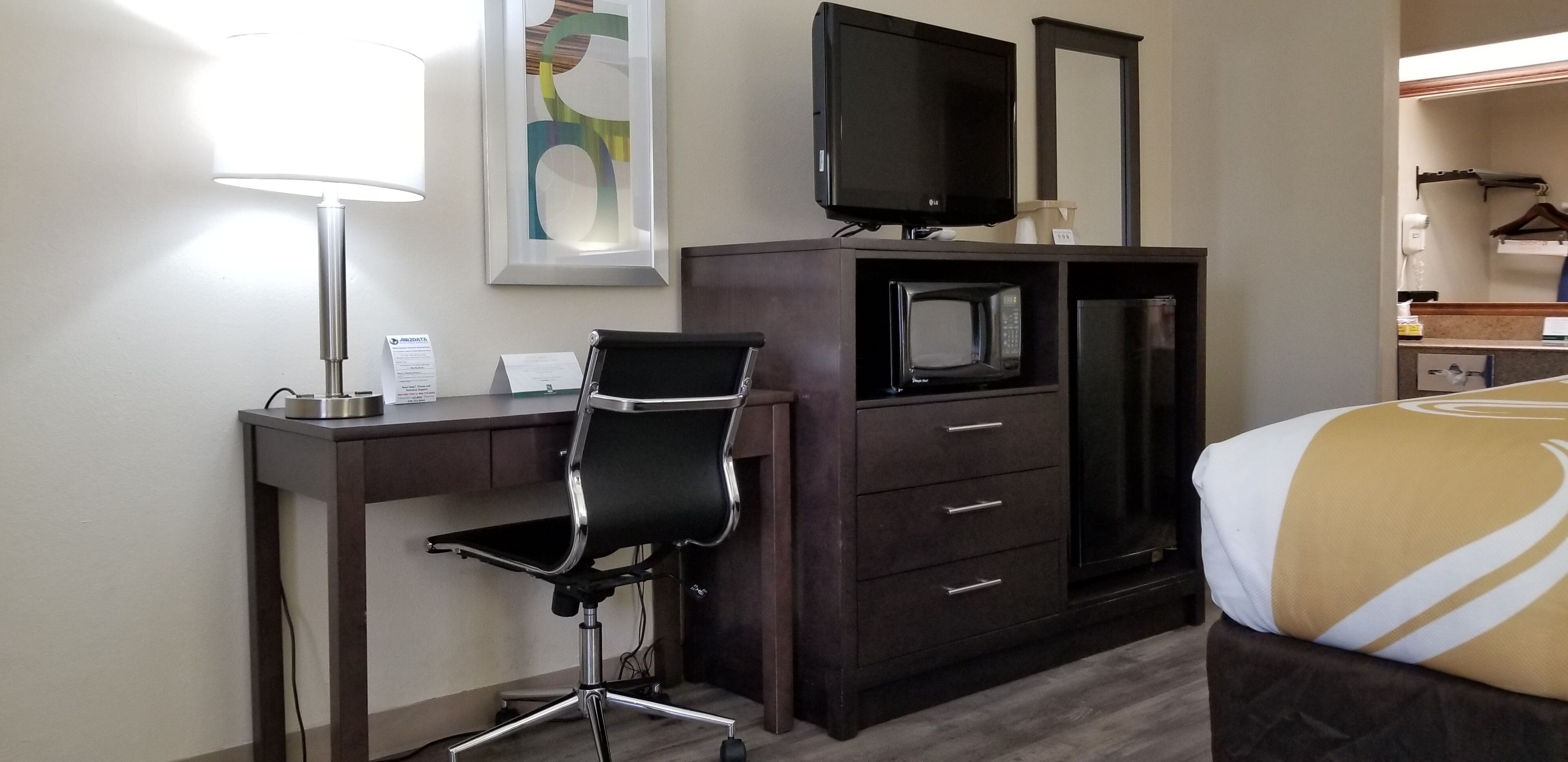 Habitación de hotel con escritorio, silla, televisión, microondas y cama.