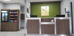 A reception area with a green wall, a sign for Quality Inn by Choice Hotels, a refrigerator stocked with snacks, and a counter with a computer and a small plant. - Quality Inn Pelham I-65 exit 246 (Pelham)