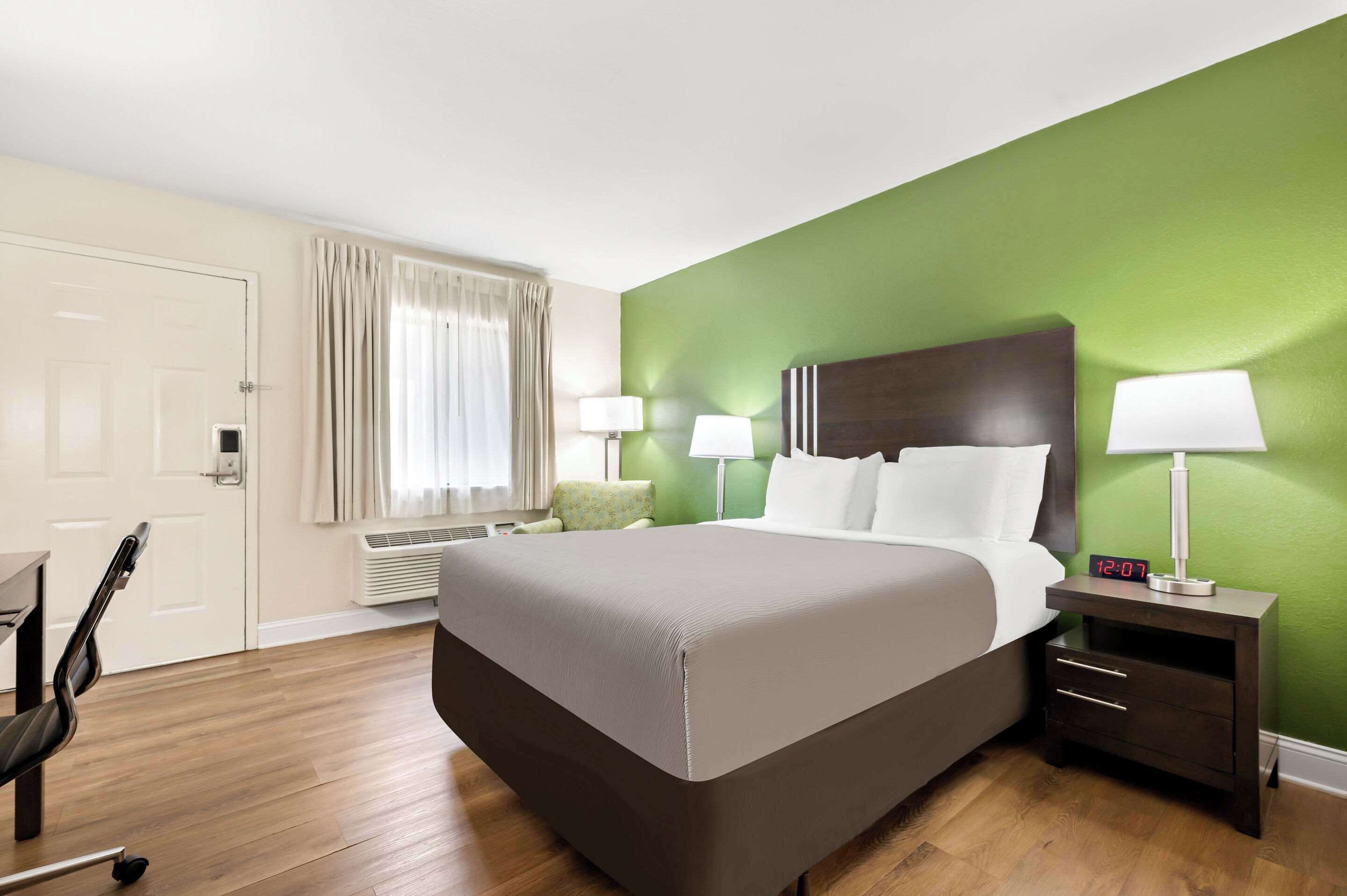 A hotel room with a large bed, two bedside tables with lamps, a chair, a desk, and a window with curtains.