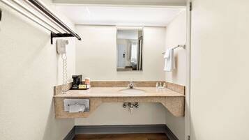 A compact bathroom with a granite countertop sink, a mirror, a towel rack, a hairdryer, and a coffee maker.