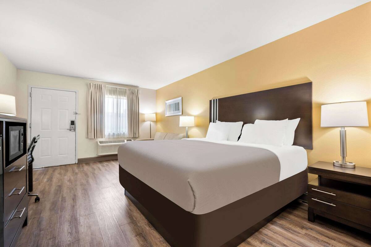 A hotel room with a large bed, bedside tables with lamps, a desk with a chair, and a door.