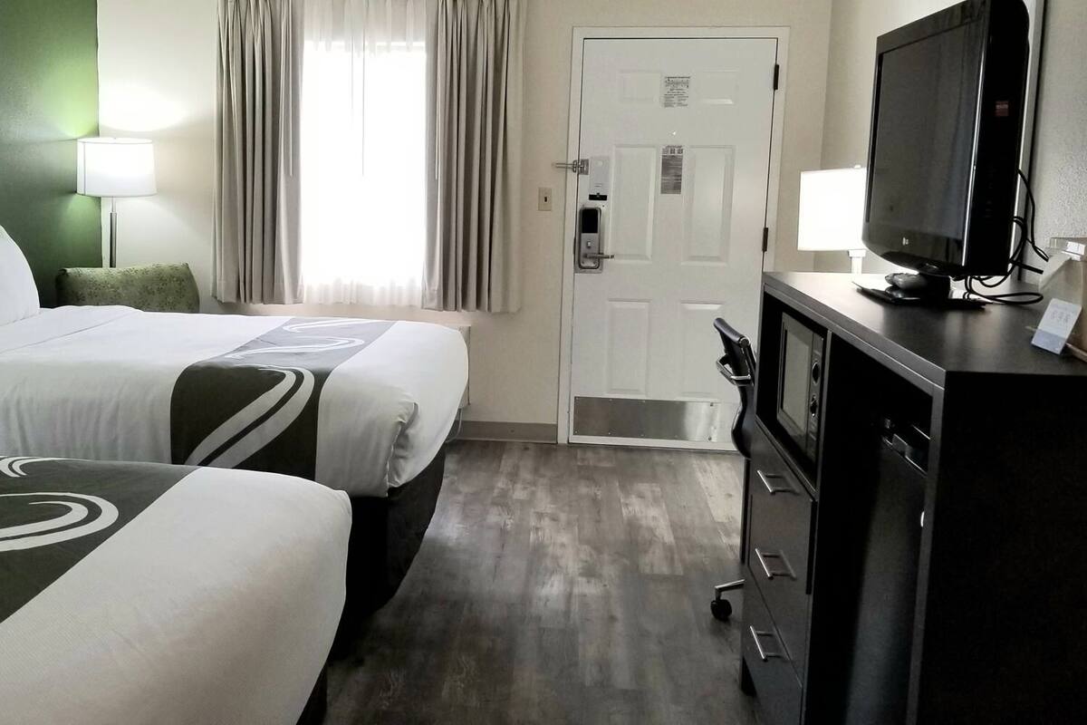 A hotel room with two beds, a television, a desk, and a door.