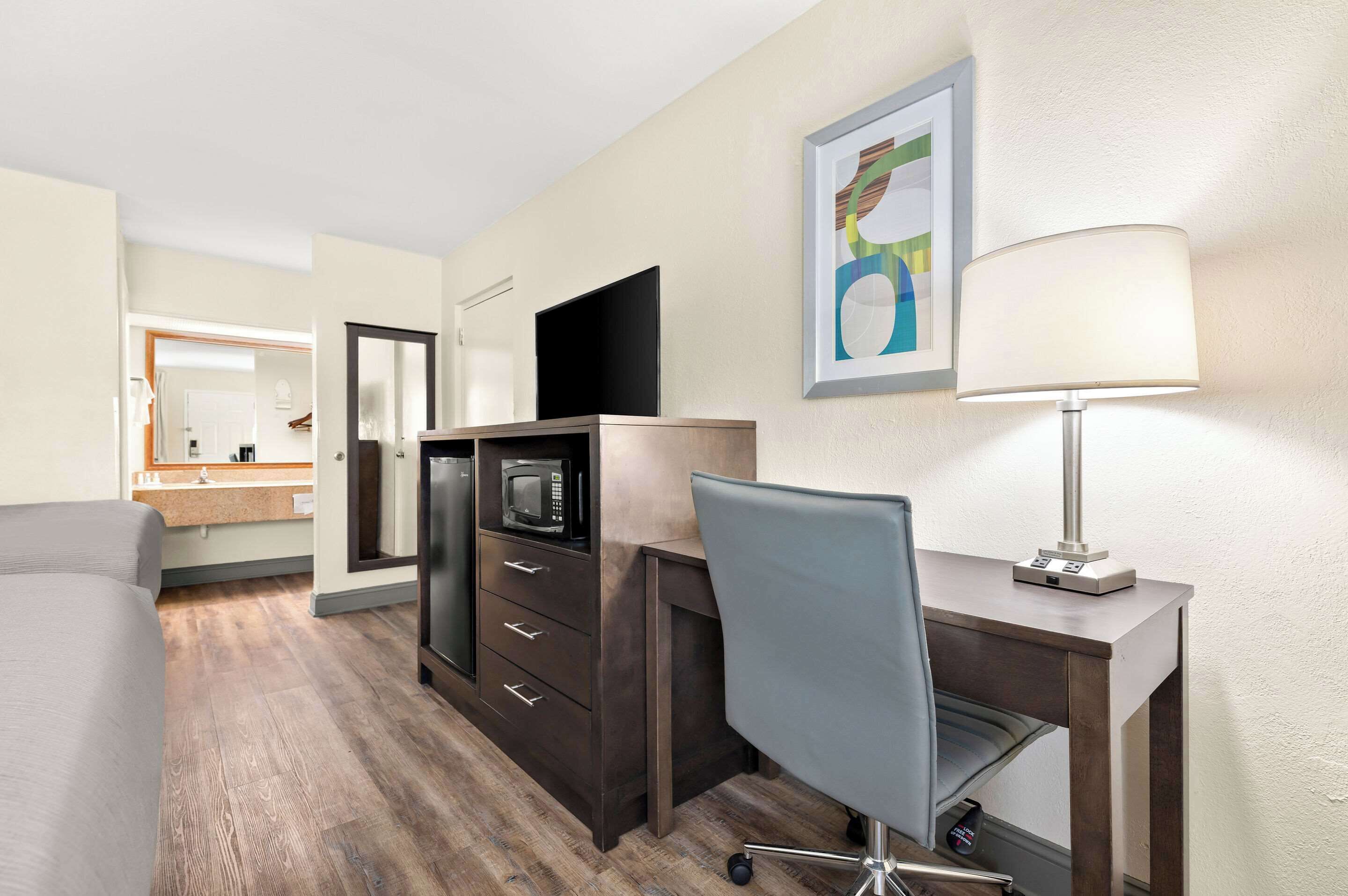 A hotel room with a bed, a desk with a chair, a microwave, a TV, and a lamp.