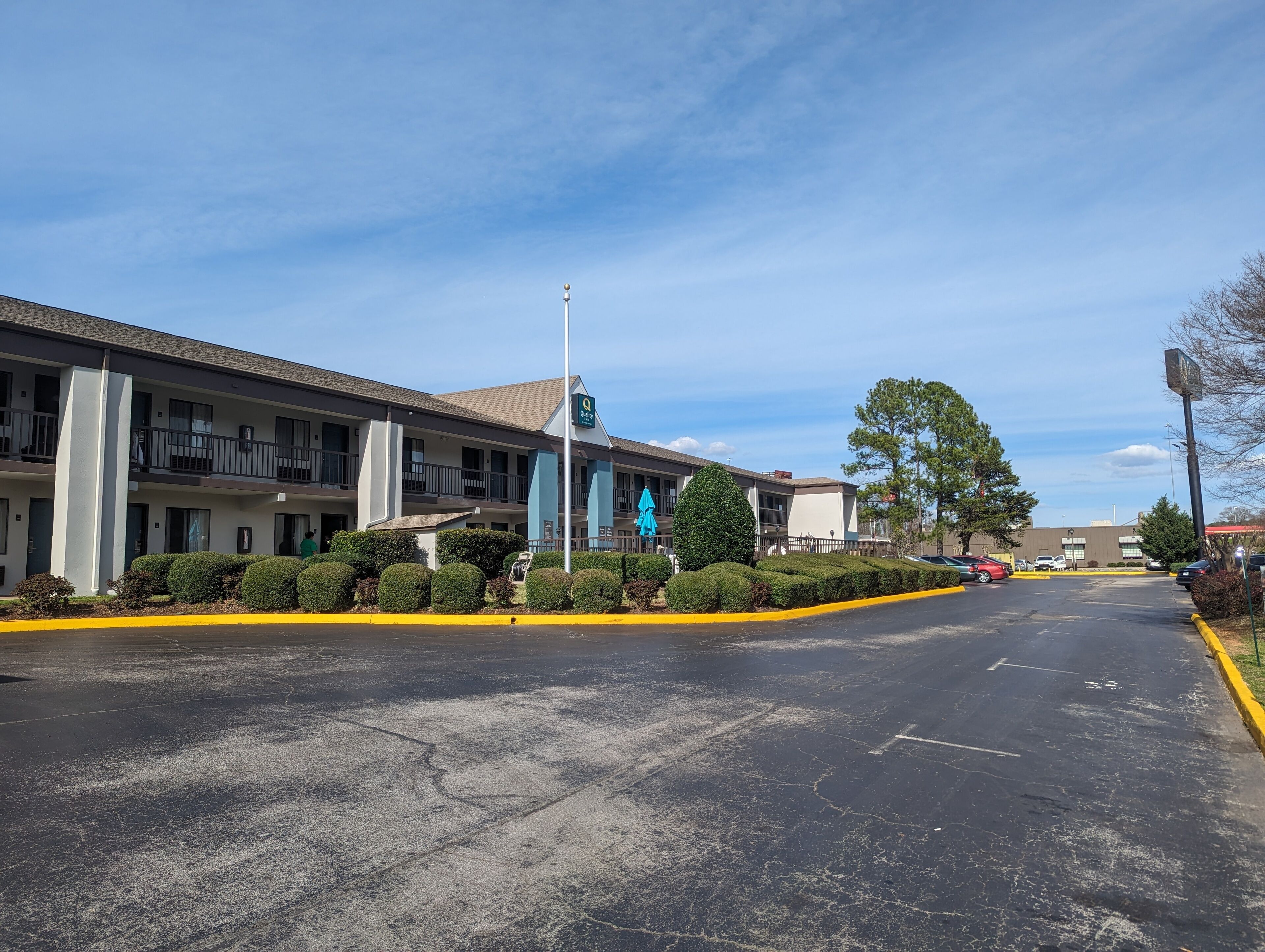 A motel with a two-story structure, a parking lot, and a clear sky.
