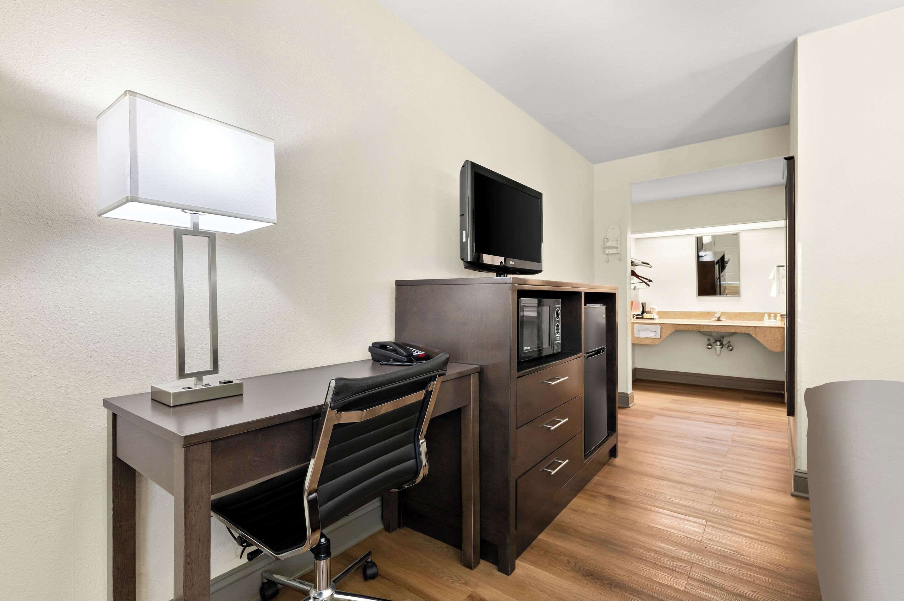 Habitación de hotel con escritorio, silla, televisor y espejo.