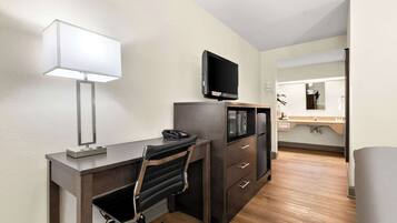 Habitación de hotel con escritorio, silla, televisor y espejo.
